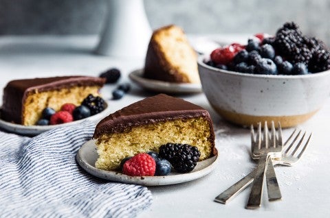Two slices of yellow cake topped with fudge frosting on plates, garnished with fresh berries