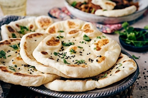 Several pieces of freshly cooked naan on a plate, garnished with herbs and ghee