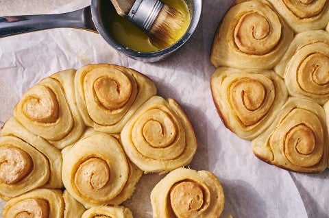 An overhead photo of Buttery Sourdough Buns with a swirl of paprika along side a small pot of melted butter with a pastry brush in it.