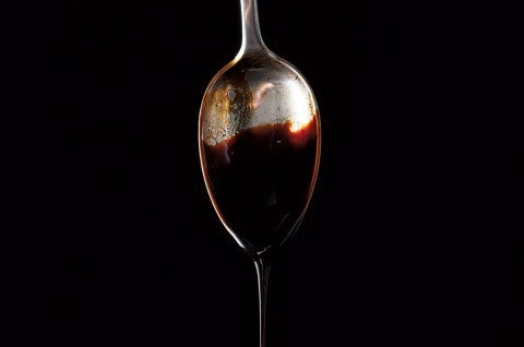 Molasses dripping off a spoon against a black background