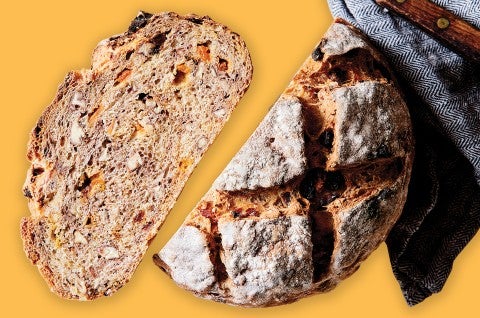 A round loaf of artisan fruit bread that has been cut in half, showing off the dense fruit-studded interior. 