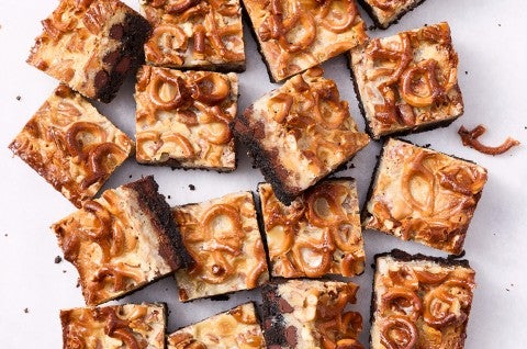 Showing a dozen gluten free chocolate seven layer bars from above with golden hues of caramel and nuts from above.