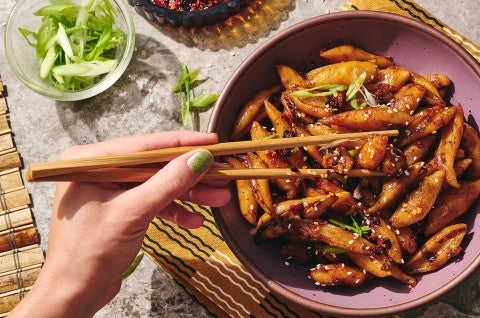 A person picking up hand cut noodles dressed with a dark umami sauce using chopsticks.