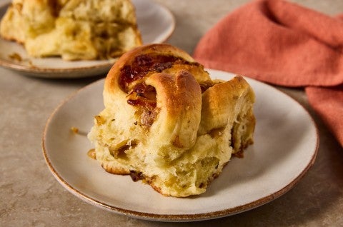 A French Onion Roll on a plate showing the golden brown exterior and lofty baked interior with caramelized onions.
