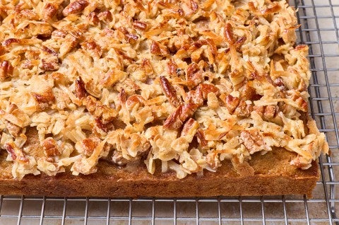 Oatmeal Cake photographed on a baking rack from the side to show a dark brown cake edge and layer of pecans, coconut, and more oats as a crunchy, toasty cap.
