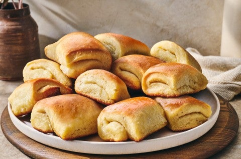 Parker house rolls stacked on a plate showing a buttery gloss and perfect folded bake.