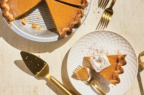 A slice of Smooth and Spicy Pumpkin Pie on a plate with the full pie in the background