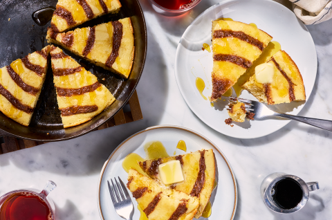 A Cinnamon Roll Skillet Pancake sliced up and shown in a cast iron skillet and also on plates.
