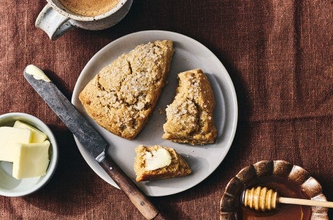Two Golden Wheat Scones on a plate, one unbroken, the other broken with a dollop of butter on it.