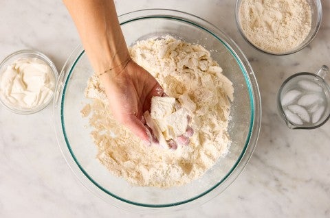 Hand holding slabs of grated butter in biscuit dough 