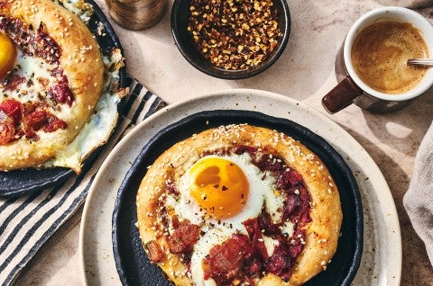 Breakfast Shakshuka shown on a plate with coffee and hot pepper flakes also in the picture.