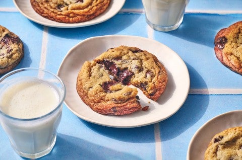 A Classic Chocolate Chip Cookie split on a plate atop a blue counter with glasses of milk in the photo.