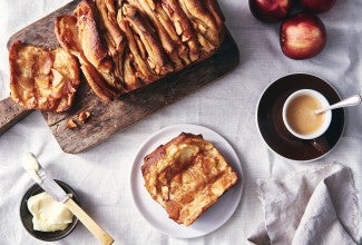 A loaf of Cinnamon Apple Pull-Apart Bread with one slice pulled off, on a plate next to a cup of coffee