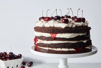 A Black Forest Cake made from layers of chocolate cake and topped with fresh cherries, on a cake stand