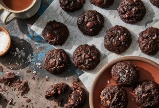 Dark chocolate brownie espresso cookies topped with flaky sea salt on a kitchen counter