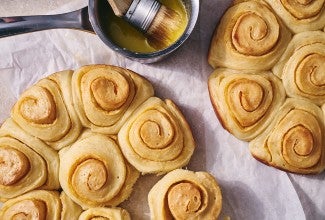 An overhead photo of Buttery Sourdough Buns with a swirl of paprika along side a small pot of melted butter with a pastry brush in it.