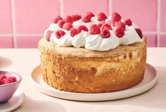 A compelte Gluten-Free Angel Food Cake topped with whipped cream and raspberries
