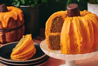 A sliced pumpkin shaped bundt cake showing layers of dark cake and orange frosting.