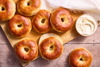 Several bagels laid out on a cutting board with a tub of cream cheese in the upper right corner of the frame.