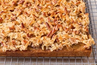 Oatmeal Cake photographed on a baking rack from the side to show a dark brown cake edge and layer of pecans, coconut, and more oats as a crunchy, toasty cap.