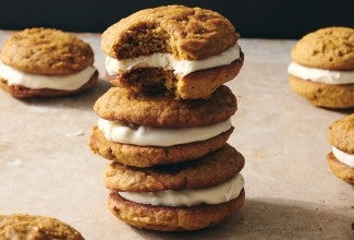 Pumpkin Whoopie Pies photographed in a stack on a counter showing the layers of pumpkin cookie and creamy filling.