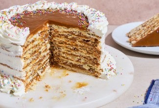 Torta Chilena photographed from the side showing a generous slice removed with layers of dulce de leche, crispy pastry, and creme fraiche frosting.