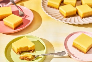 A table set with pastel colored tableware and plates with Passionfruit Bars spread out.