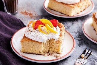 A slice of Tres Leches Cake topped with whipped cream on a plate