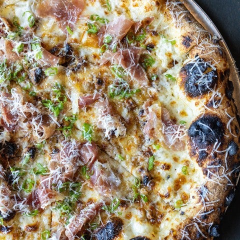 Overhead shot of a pizza covered in delectable toppings with darkened woodfired areas of the crust. - select to zoom
