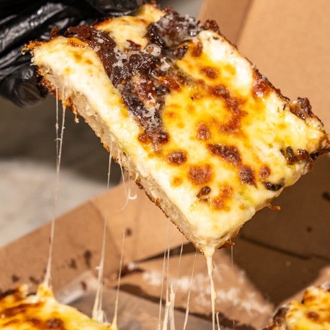 A hand lifting a square slice of pizza out of a pizza box with cheese dripping down. - select to zoom