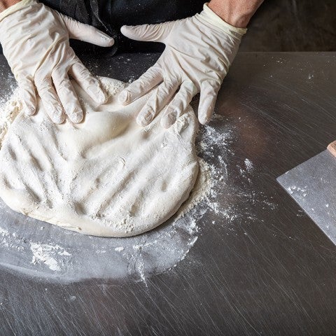 Photograph of hands kneading pizza dough that's covered in flour on a counter. - select to zoom