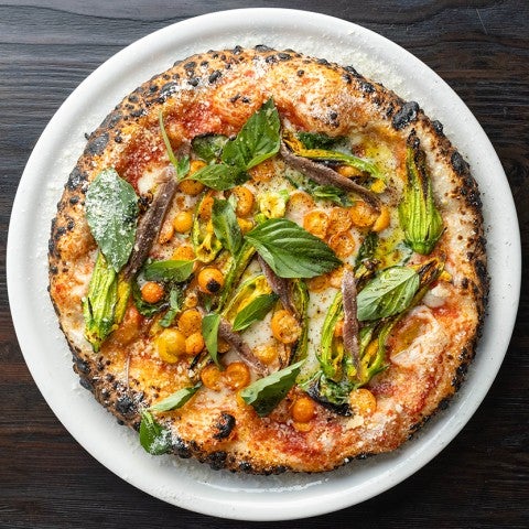 Photograph of a wood fired pizza from above sitting on a white plate on a dark table. - select to zoom