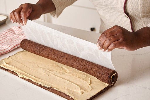 Using parchment underneath a frosted chocolate sheet cake to roll it into a cylinder.