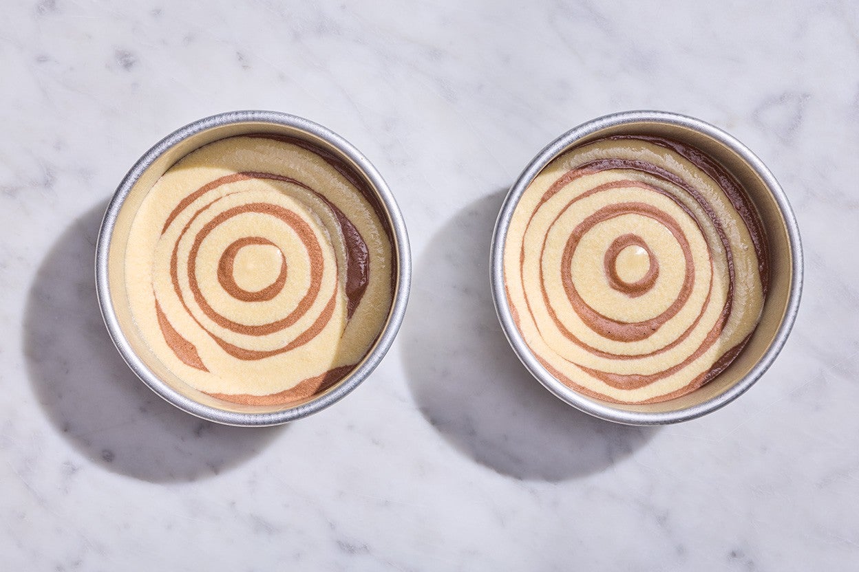 Souche de Noël cake batter in two round pans with vanilla and chocolate cake batter swirled to make a marbled cake.