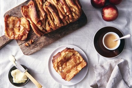 A loaf of Cinnamon Apple Pull-Apart Bread with one slice pulled off, on a plate next to a cup of coffee