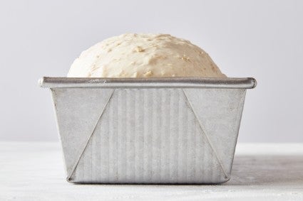 Pan loaf bread dough rising above the rim of the pan
