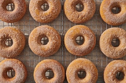 A dozen baked pumpkin donuts on a cooling rack.