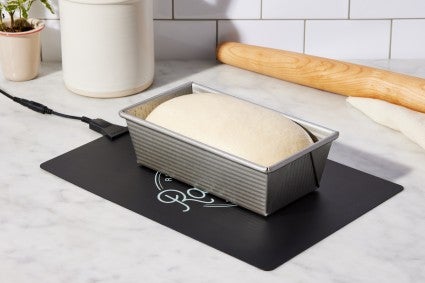 Loaf pan of proofing bread dough on dough riser