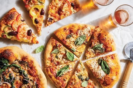 A large round pizza on a marble counter, garnished with fresh basil and cut into six pieces