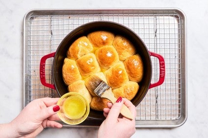Brush melted butter over baked dinner rolls in Dutch oven