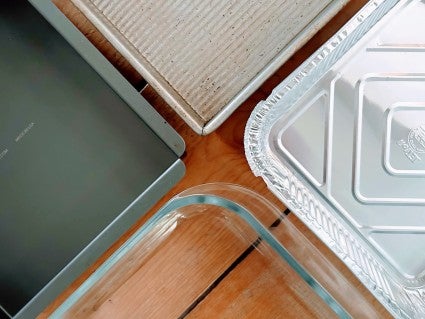 Four different 9" square pans: black aluminum, dark gray steel-aluminum, disposable tinfoil, and clear tempered glass. 