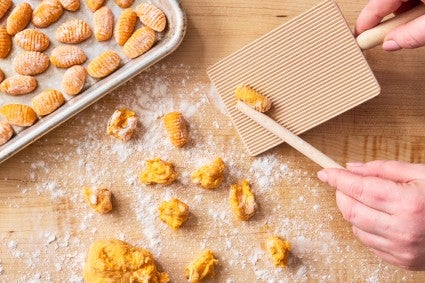 Hands shaping sweet potato gnocchi dough with a gnocchi board
