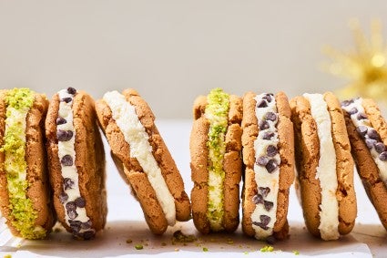 A lineup of cannoli sandwich cookies showing the cookies, a layer of filling, and chocolate chips or pistachio coating.