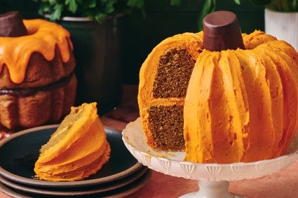 A sliced pumpkin shaped bundt cake showing layers of dark cake and orange frosting.