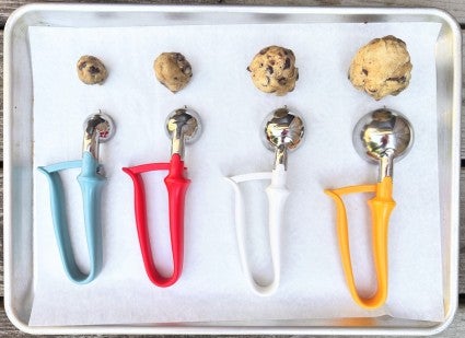 Cookie scoops and balls of cookie dough on a parchment-lined baking sheet.