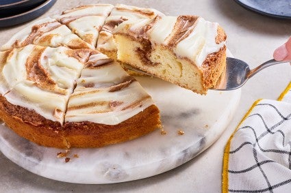 Removing a slice of Cinnamon Roll Cake from the cake showing the cinnamon sugar layer inside the golden cake and the icing on top.