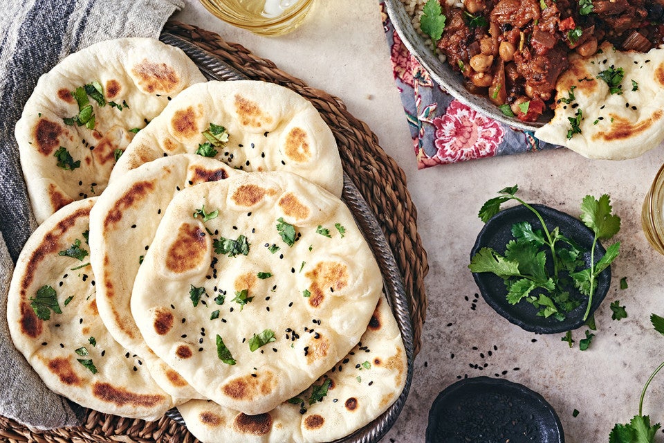 Freshly baked Naan bread in a basket next to a bowl of herbs and chutney