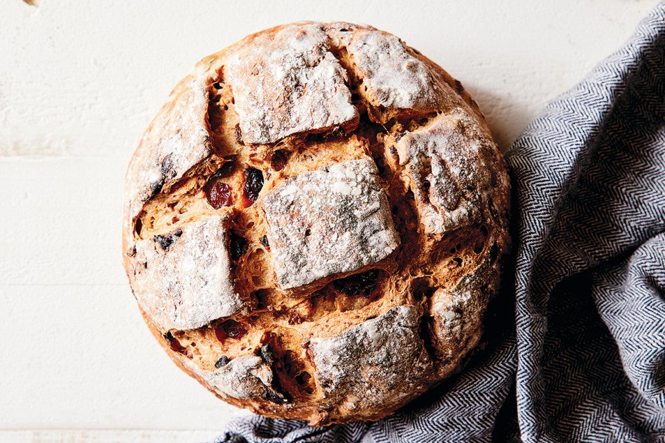 An artisan fruit bread with a crusty exterior and checkerboard pattern scored into the top. 