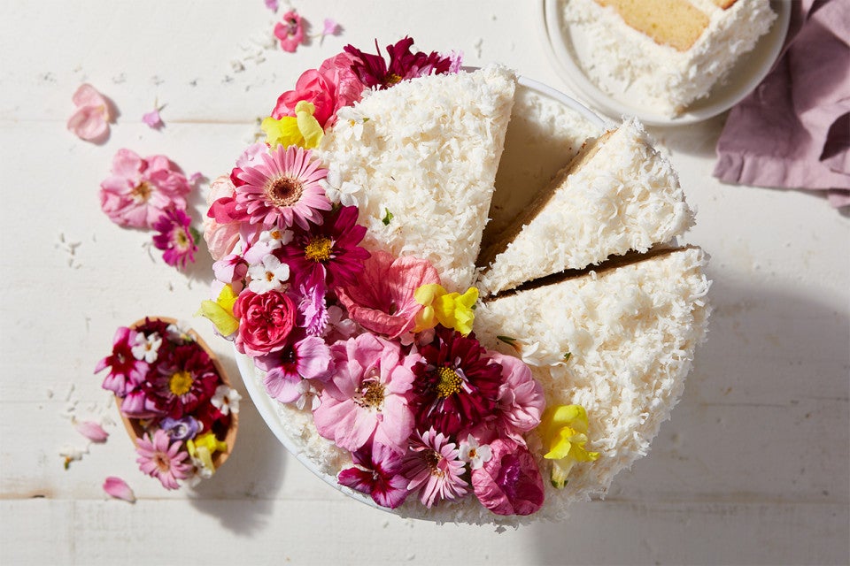 A Old-Fashioned Coconut Cake coated in shredded coconut and decorated with a spray of edible flowers