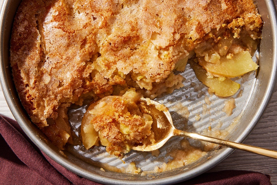 A close-up shot a round pan of Sugar-Crusted Apple Cobbler with a spoonful portioned